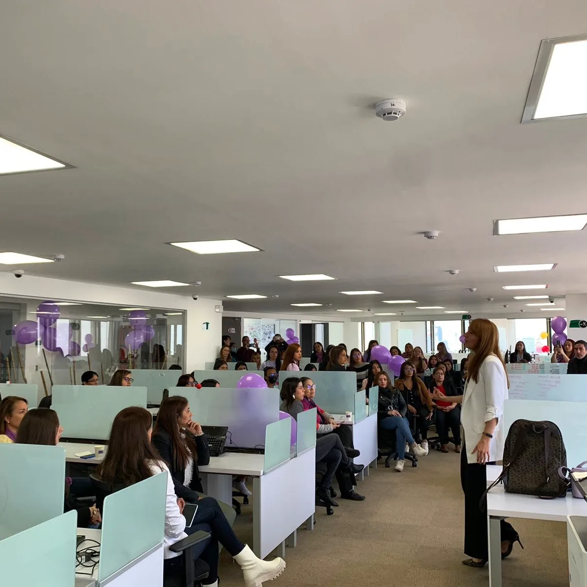 Catalina dictando una conferencia con audiencia y globos lilas