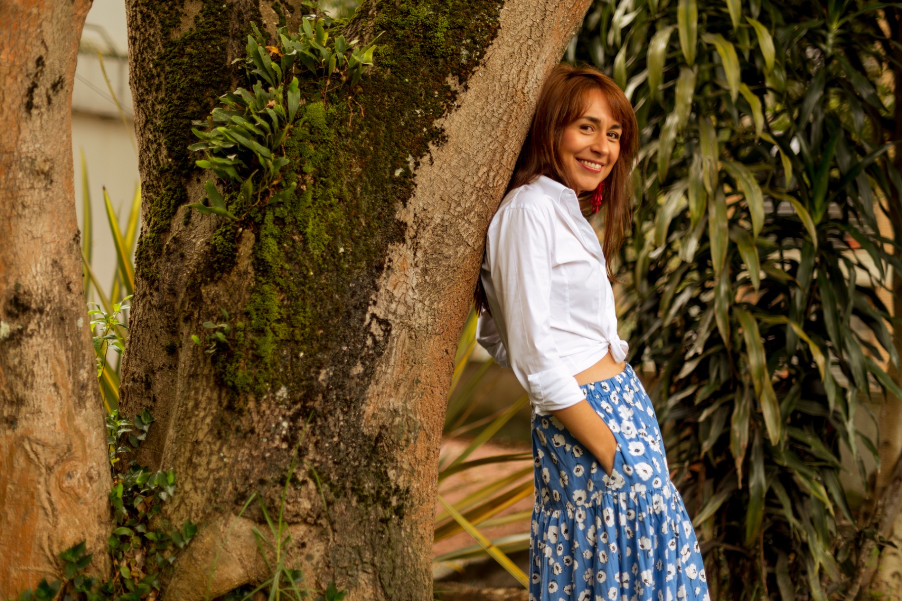 Catalina Vega sonriendo, apoyada en un árbol entre vegetación